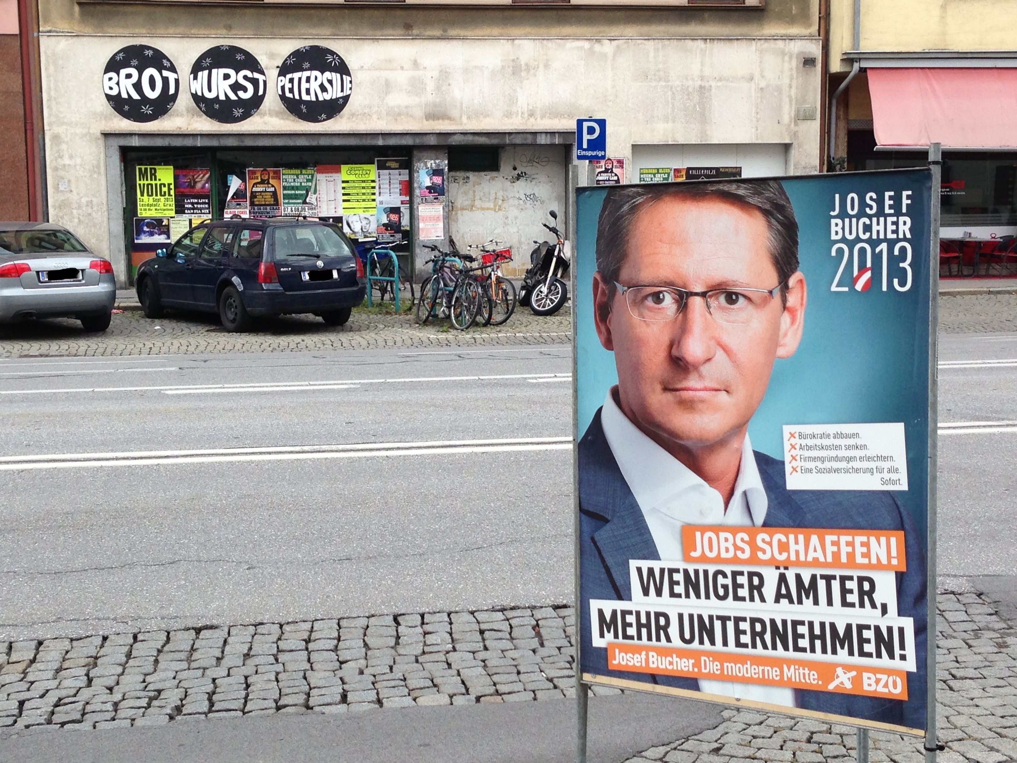 Die Wahlplakate nutzen die letzten freien Flächen im öffentlichen Raum. Im Hintergrund sieht man ein Kunstwerk von Bernhard Wolf, das einen Moment die Aufmerksamkeit von der Werbung wegziehen soll.