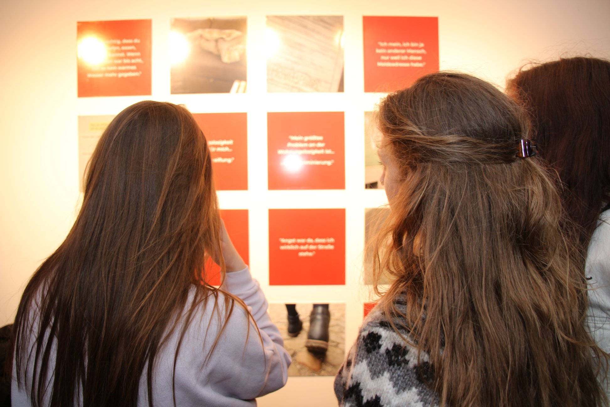 Drei Personen schauen sich die Ausstellung "Ich bin da. Wohnungslosigkeit ist auch weiblich” an.