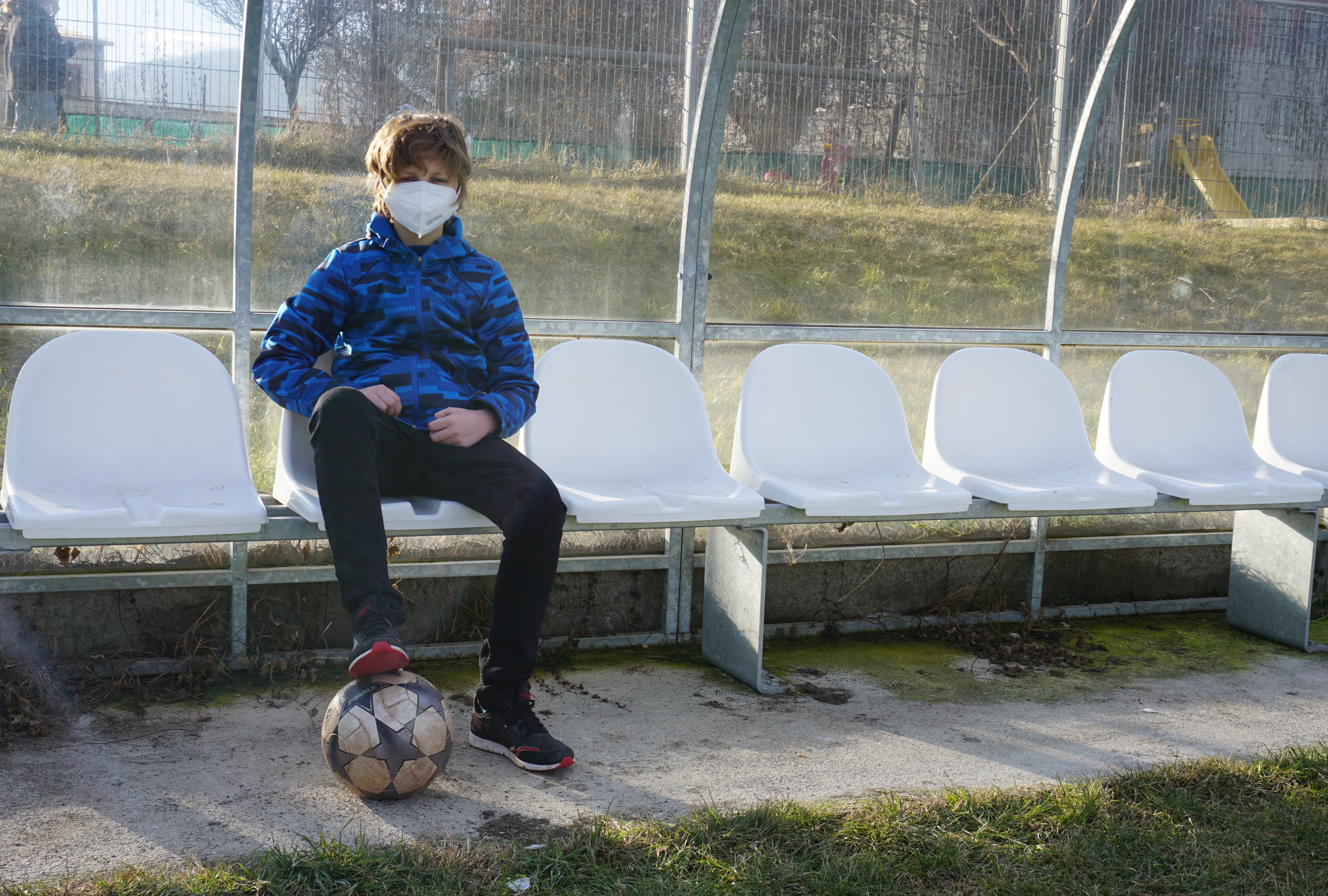 Spieler Nino sitzt allein auf der Trainerbank mit Ball am Fuß.