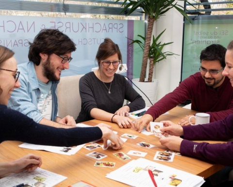 Fünf Menschen sitzen an einem Tisch und lernen mittles Kartenspiel den steirischen Dialekt.