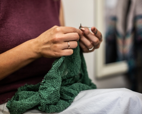 Eine Dame strickt einen grünen Pullover.