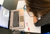 Ein Mädchen sitzt an einem Arbeitsauftrag neben ihrem Laptop.