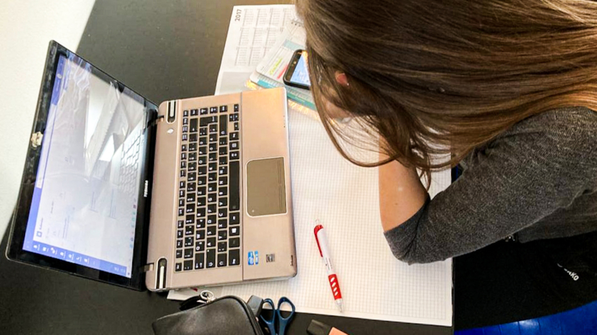 Ein Mädchen sitzt an einem Arbeitsauftrag neben ihrem Laptop.