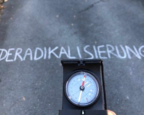 Ein Kompass zeigt mit der roten Nadel in Richtung des Schriftzuges "Deradikalisierung"