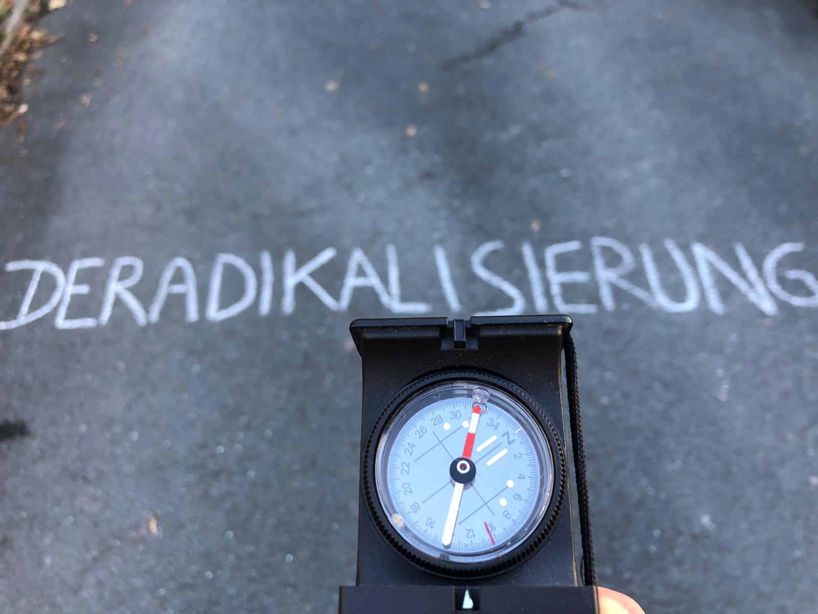 Ein Kompass zeigt mit der roten Nadel in Richtung des Schriftzuges "Deradikalisierung"