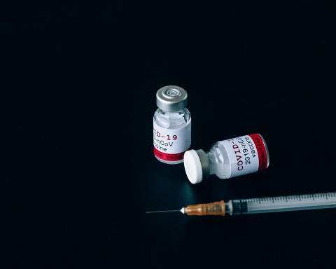 Zwei Covid-19 Impfdosen, mit Spritze auf schwarzem Hintergrund