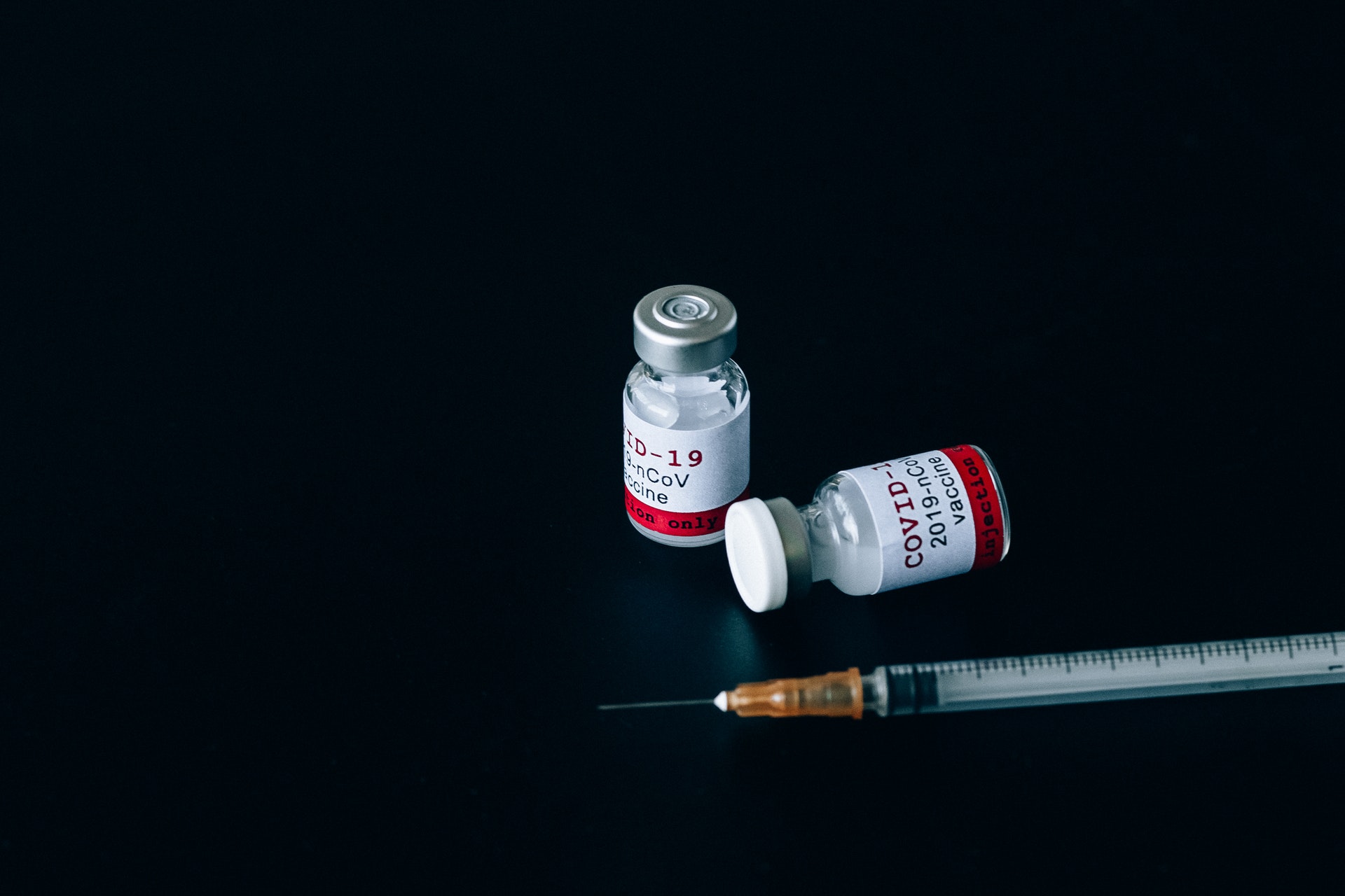 Zwei Covid-19 Impfdosen, mit Spritze auf schwarzem Hintergrund