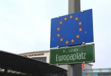 Dunkelgrünes Straßenschild am Europaplatz, darüber die EU-Fahne blau mit 12 gelben Sternen
