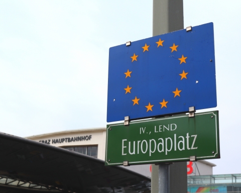 Dunkelgrünes Straßenschild am Europaplatz, darüber die EU-Fahne blau mit 12 gelben Sternen