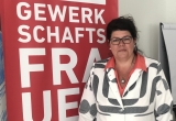 Helga Ahrer steht vor einem roten Banner mit der Aufschrift „Gewerkschaftsfrauen".