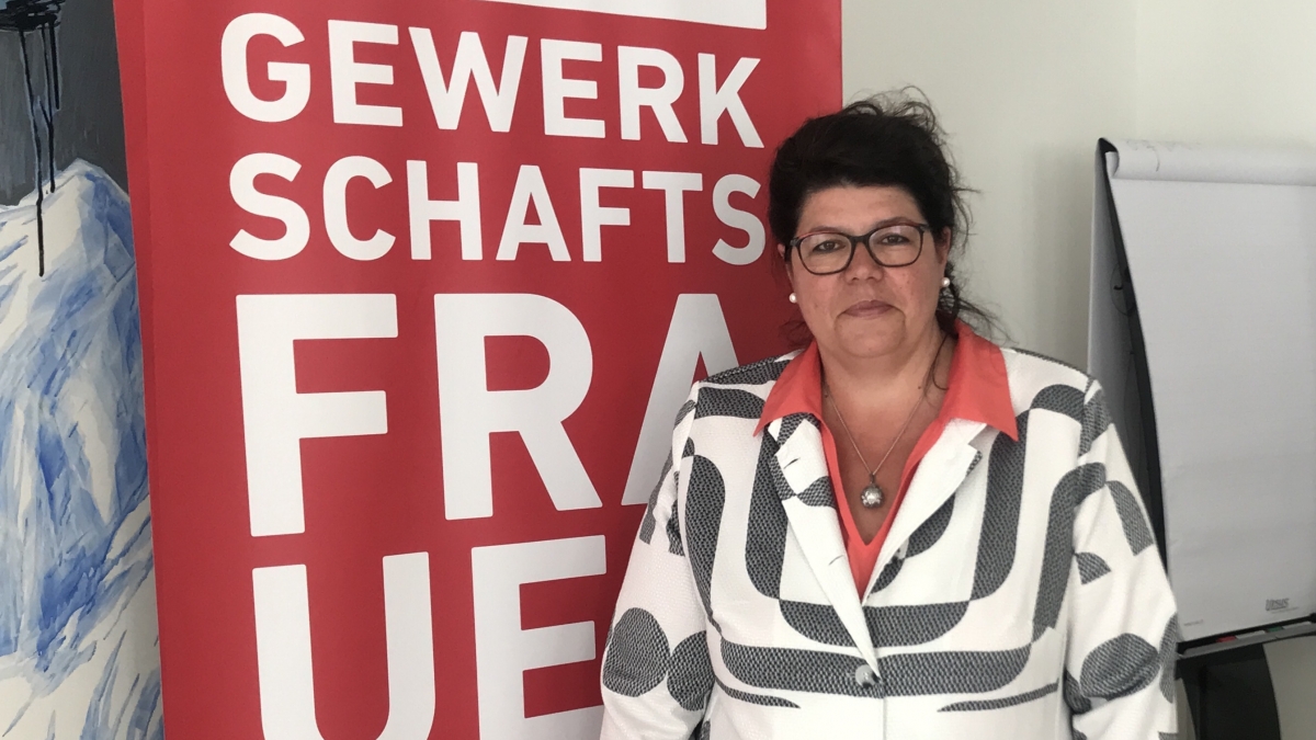 Helga Ahrer steht vor einem roten Banner mit der Aufschrift „Gewerkschaftsfrauen".