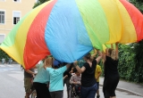 Unter einer Plane stehen Kinder des Mosaik Schulheims und Kinder des Schülerhorts Fröbelpark und spielen gemeinsam
