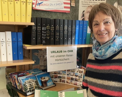 Die Leiterin der HörBibliothek vor dem Regal, das mit Reise-Hörbüchern bestellt ist