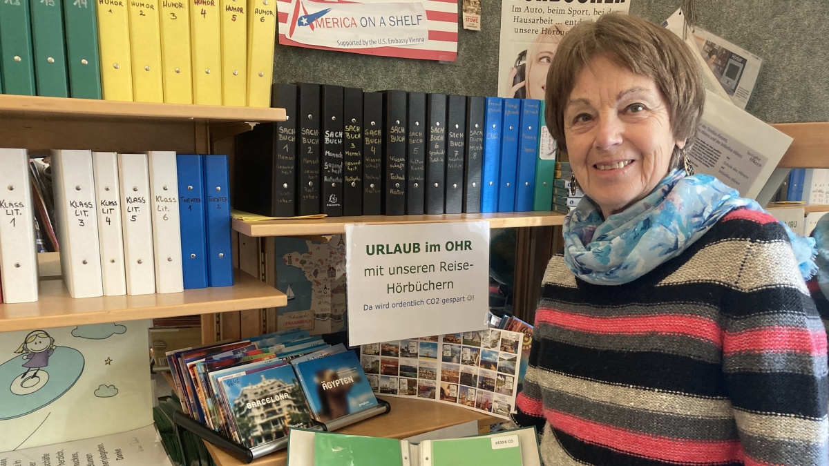 Die Leiterin der HörBibliothek vor dem Regal, das mit Reise-Hörbüchern bestellt ist