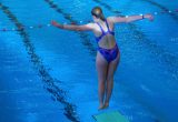 Eine junge Wasserpringerin steht am Sprungbrett und ist für den Absprung ins Wasser bereit.