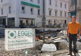 Johann Winkler steht vor einem Bauzaun. Dahinter sind die Enden der neu gebauten Gleise in der Vorbeckgasse zu sehen. Hinter dieser Baustelle liegt das Geschäft Egger & Co.