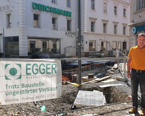 Johann Winkler steht vor einem Bauzaun. Dahinter sind die Enden der neu gebauten Gleise in der Vorbeckgasse zu sehen. Hinter dieser Baustelle liegt das Geschäft Egger & Co.