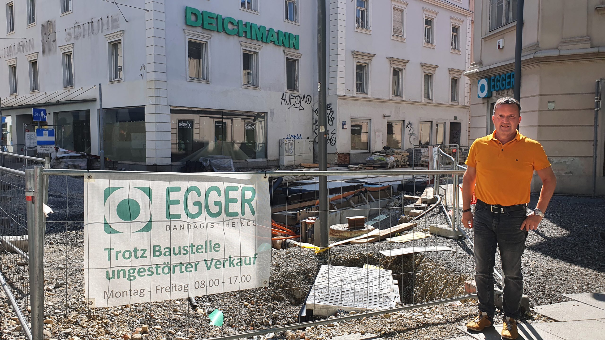 Johann Winkler steht vor einem Bauzaun. Dahinter sind die Enden der neu gebauten Gleise in der Vorbeckgasse zu sehen. Hinter dieser Baustelle liegt das Geschäft Egger & Co.