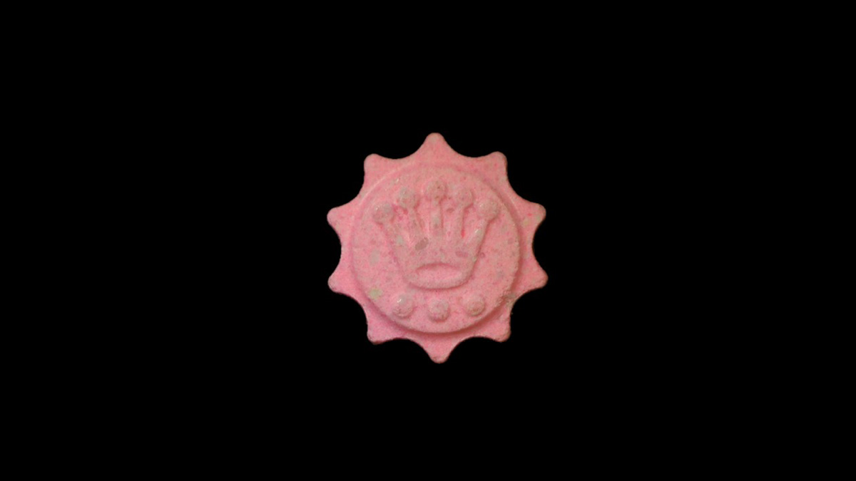 Eine rosa Pille mit einem Kronensymbol auf schwarzem Hintergrund.