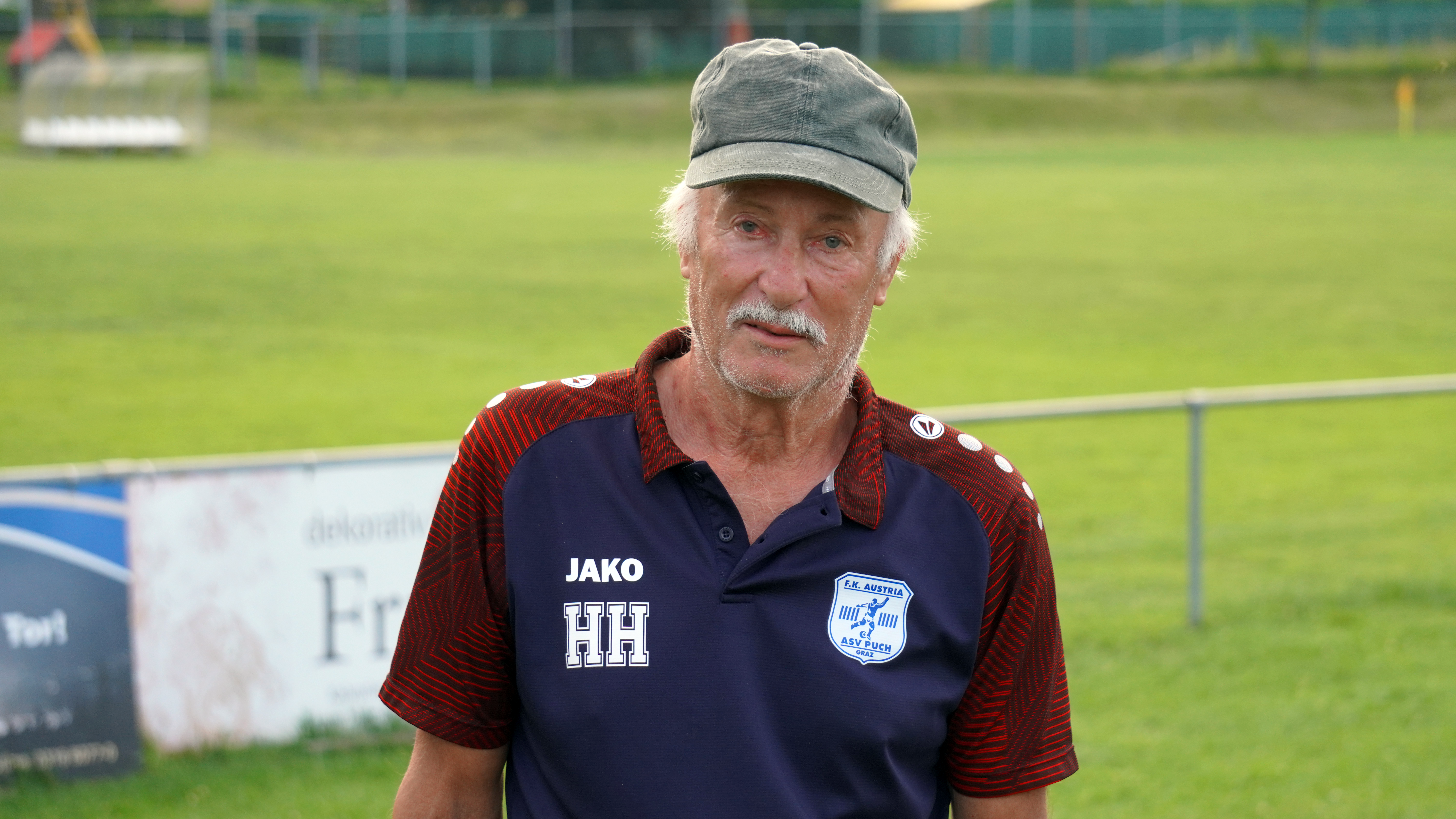 Der Obmann von Austria Puch. Alfred Horner steht vor dem Spielfeld in seinem Vereinsshirt.