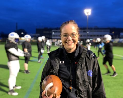 Marie steht vor den Spielern, die sie trainiert, und hält einen Football in der Hand.