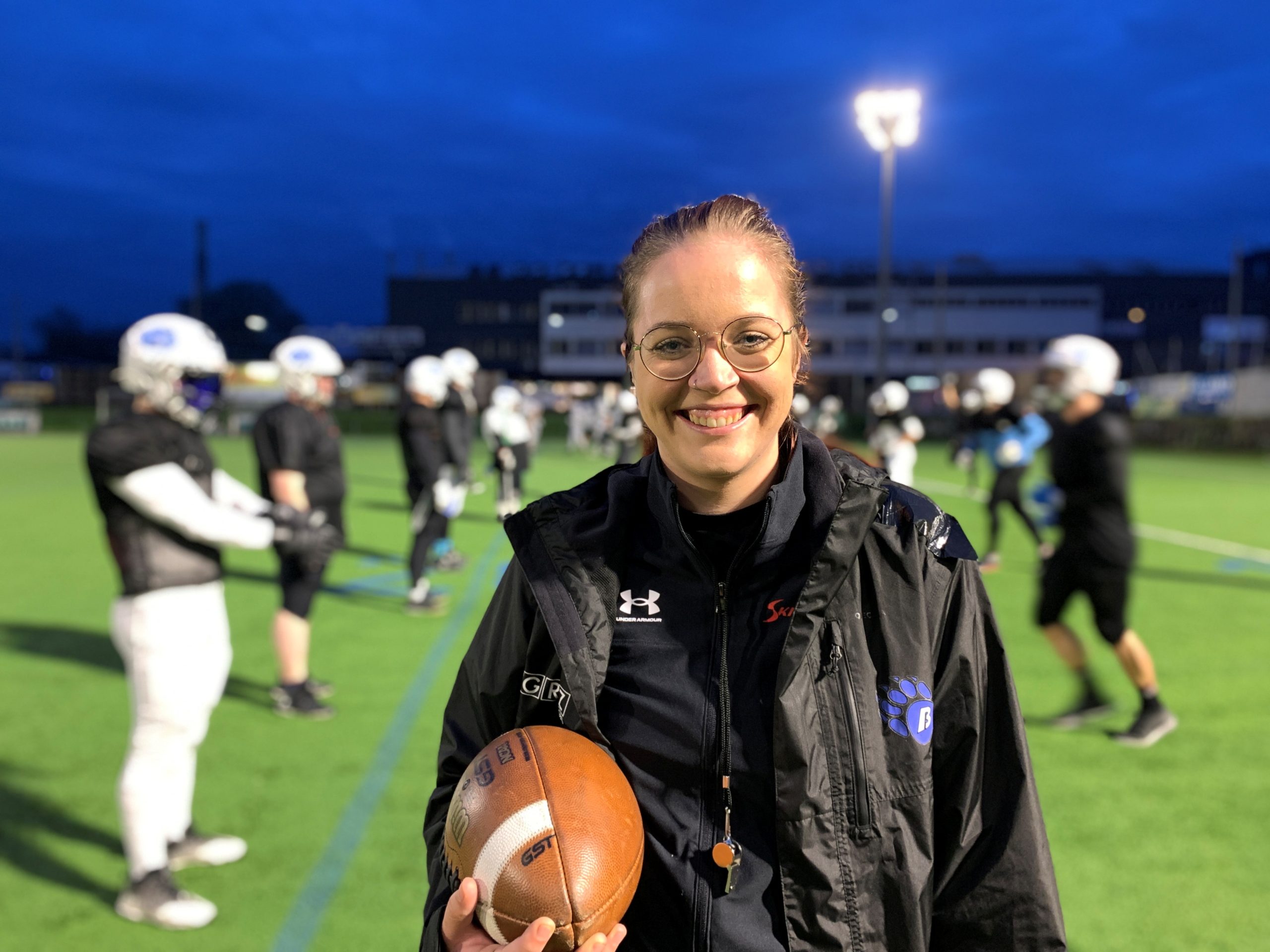 Marie steht vor den Spielern, die sie trainiert, und hält einen Football in der Hand.