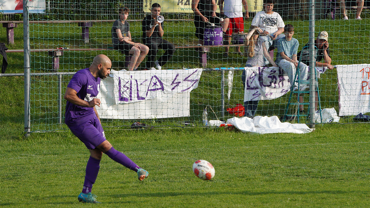 Karim Shafei beim Zuspiel. Er ist mitten in der Bewegung, hat den Ball erst vor wenigen Augenblicken getroffen. Im Hintergrund sieht man die Fans der Mannschaft mit Bannern, Trommel und Megafon.