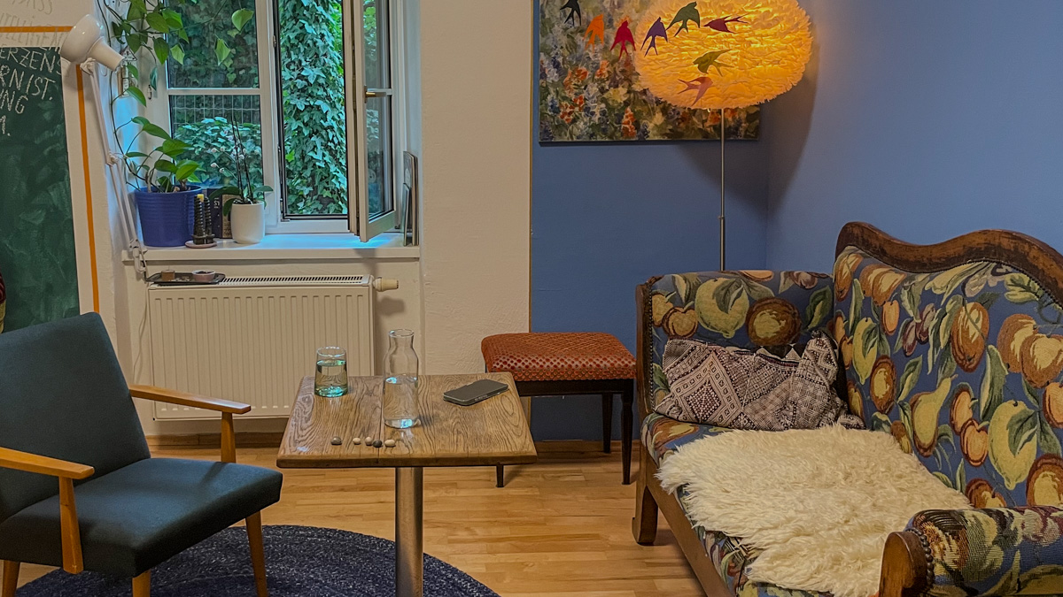 Im Büro der Trauma-Beraterin befindet sich ein gemustertes Sofa, eine Stehlampe, ein Beistelltisch und ein Sessel. 