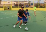 Zwei Fußballspieler mit Augenbinden kämpfen um einen Ball. Sie stehen auf einem Sportplatz mit grünem Belag und gelben Banden. Im Hintergrund stehen noch andere Spieler.