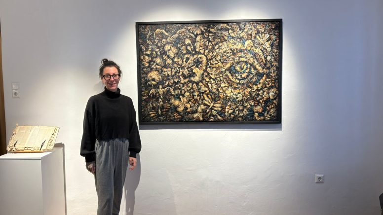 Künstlerin Helga Kovacs steht neben einem ihrer Kunstwerke, das an der Wand in der Galerie Papst hängt.