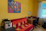 Rotes Sofa steht vor gelber Wand. Darüber hängt ein buntes Bild.