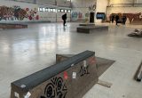 Die neue Skaterhalle. Ein mit Graffiti besprühtes Hindernis steht im Vordergrund. Im Hintergrund ist klein noch eine Person von hinten zu sehen.