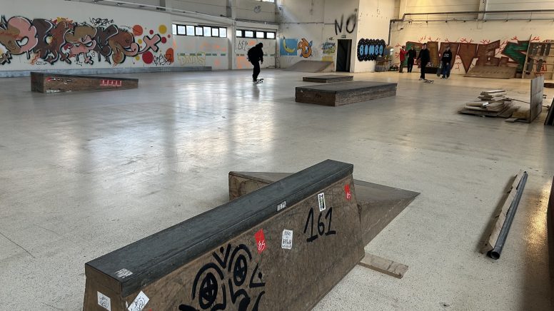 Die neue Skaterhalle. Ein mit Graffiti besprühtes Hindernis steht im Vordergrund. Im Hintergrund ist klein noch eine Person von hinten zu sehen.