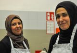 Die Küchengehilf:innen Meral Khan und Naile Kya stehen in der Küche und lächeln in die Kamera.
