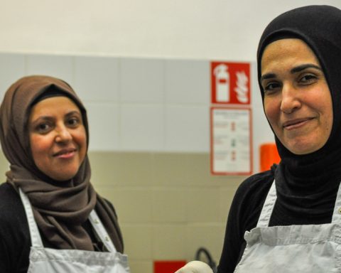 Die Küchengehilf:innen Meral Khan und Naile Kya stehen in der Küche und lächeln in die Kamera.