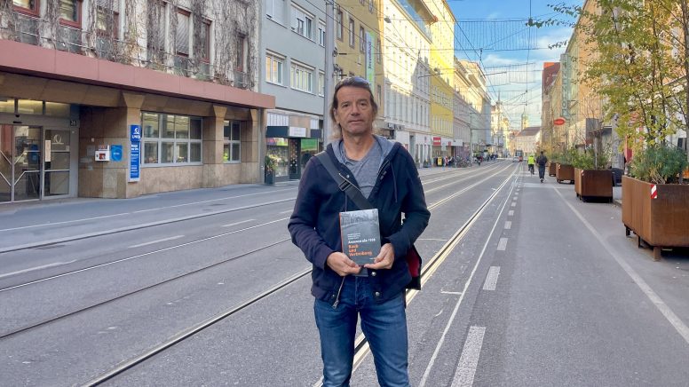 Der Autor Heimo Halbrainer steht in der Annenstraße und hält das Buch in der Hand.