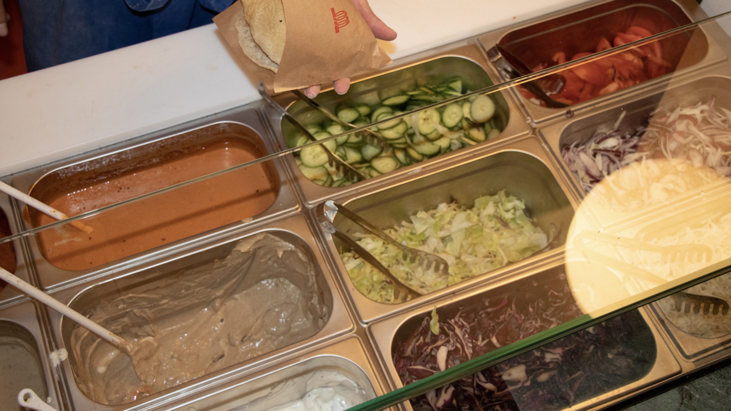 Eine Theke gefüllt mit Gurken, Tomaten, Zwiebeln, Salat, Rotkraut und Saucen.