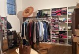 Zu sehen ist ein Regal, das mit Klamotten gefüllt ist sowie einige Kleiderständer.