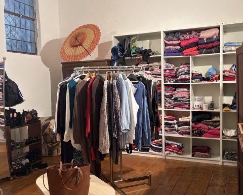 Zu sehen ist ein Regal, das mit Klamotten gefüllt ist sowie einige Kleiderständer.