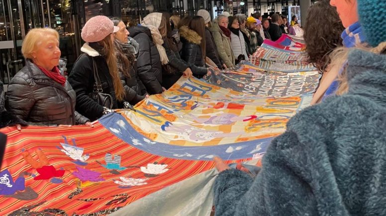 Gemeinschaftlich wird von Besuchern ein selbtsgemachtes Banner in die Luft gehalten, das auf die gewalt an Frauen aufmersam machen soll.
