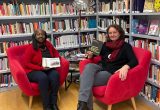 Auf dem Bild sind zwei Frauen vor einem großen Bücherregal mit feministischen Schriften. Die Frauen sind Petra Leschanz vom Verein Frauenservice und Edith Abawe vom Infocafe Palaver.