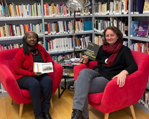 Auf dem Bild sind zwei Frauen vor einem großen Bücherregal mit feministischen Schriften. Die Frauen sind Petra Leschanz vom Verein Frauenservice und Edith Abawe vom Infocafe Palaver.