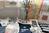 Ein Tisch mit einem Osterstrauß mit bunt verzierten Eiern. Bedruckte Taschen mit verschiedensten Mustern. Brillenetuis und Schlüsselanhänger kunstvoll bemalt