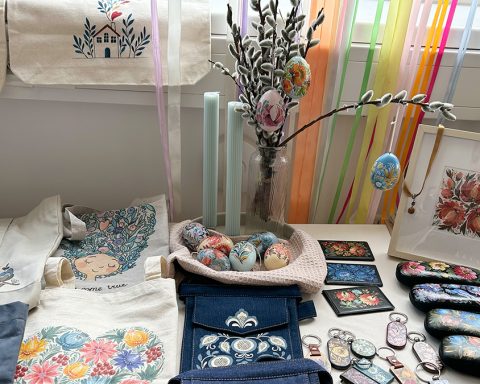 Ein Tisch mit einem Osterstrauß mit bunt verzierten Eiern. Bedruckte Taschen mit verschiedensten Mustern. Brillenetuis und Schlüsselanhänger kunstvoll bemalt