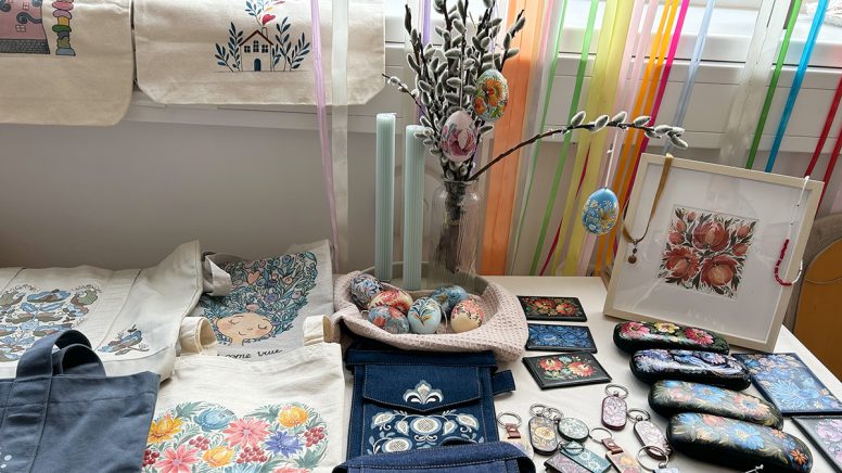 Ein Tisch mit einem Osterstrauß mit bunt verzierten Eiern. Bedruckte Taschen mit verschiedensten Mustern. Brillenetuis und Schlüsselanhänger kunstvoll bemalt