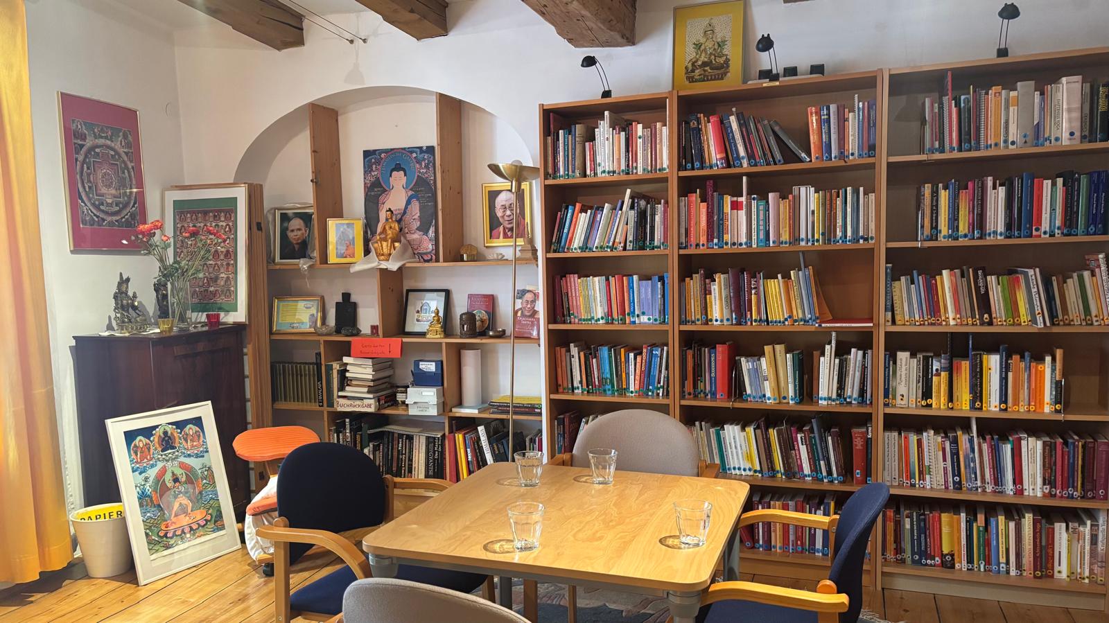 Foto eines Raumes, bunte Bücher gestapelt in einem Regal, ein Tisch mit vier Sesseln