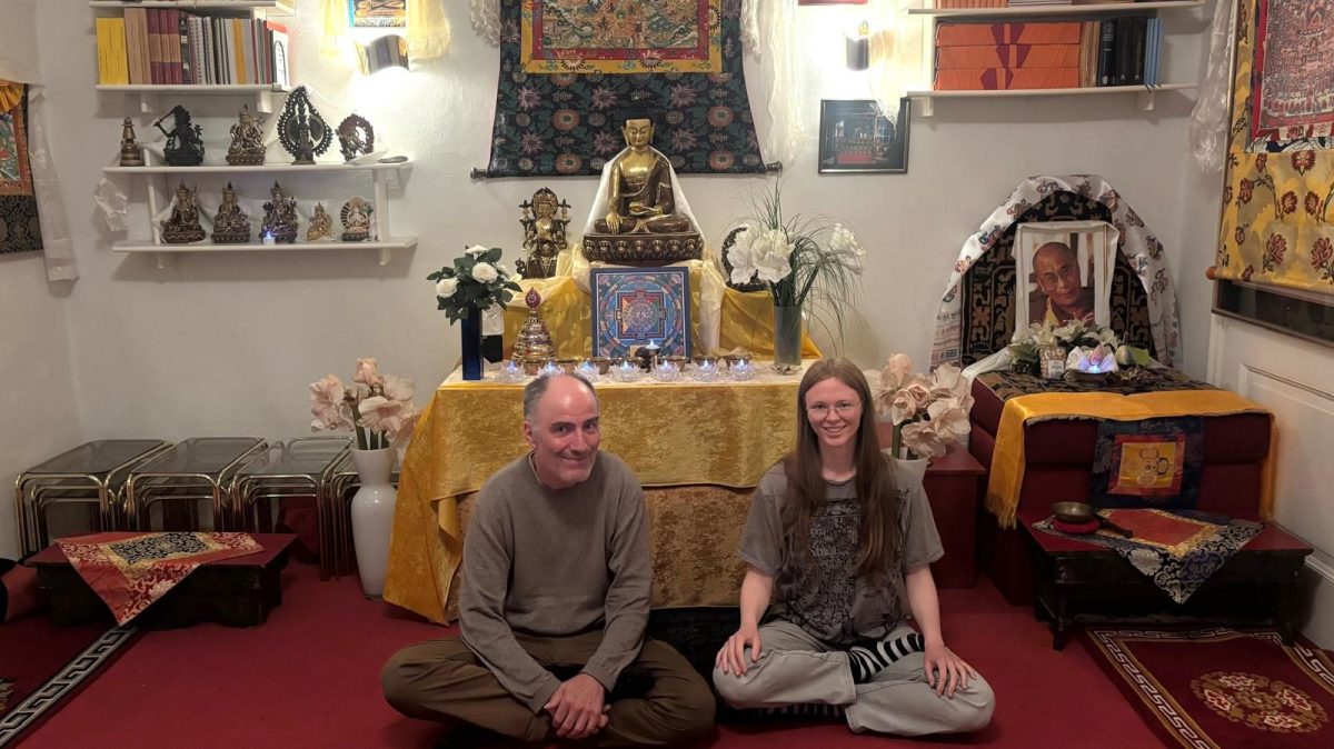 Ein älterer Mann und eine junge Frau sitzen in einem farbenfrohen Raum vor einem buddhistischen Altar.